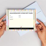 woman's hands holding a Kaleidoscope Living Gift Card with an open blue envelope in the background