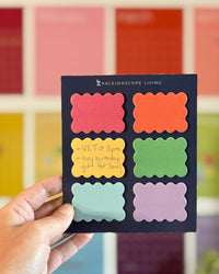Colorful sticky notes with scalloped edges on navy blue backing held up with a hand