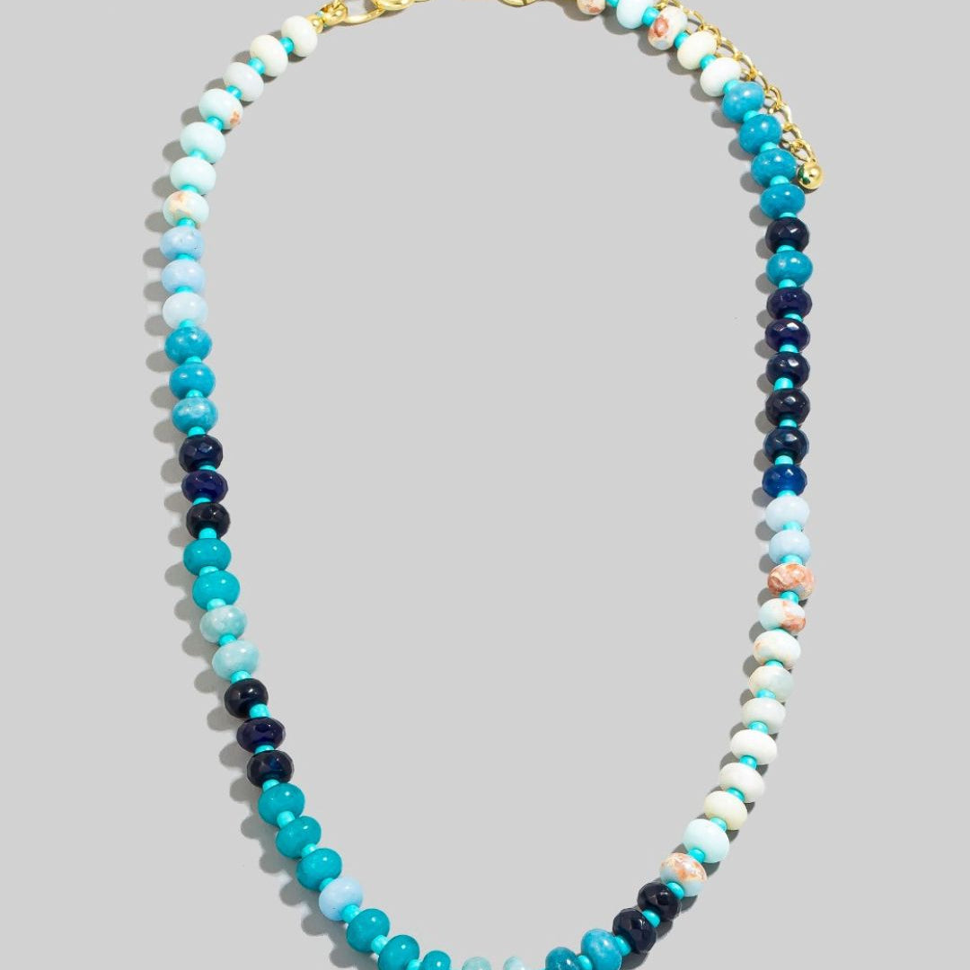 A beaded necklace with a gradient of natural stone beads in shades of white and blue, with gold-colored metal clasp and extender chain.