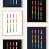 Framed art prints featuring minimalist illustrations of Clothespins in rainbow hues on black, navy blue and white backgrounds.