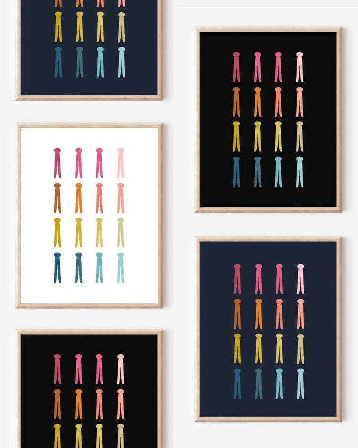 Framed art prints featuring minimalist illustrations of Clothespins in rainbow hues on black, navy blue and white backgrounds.