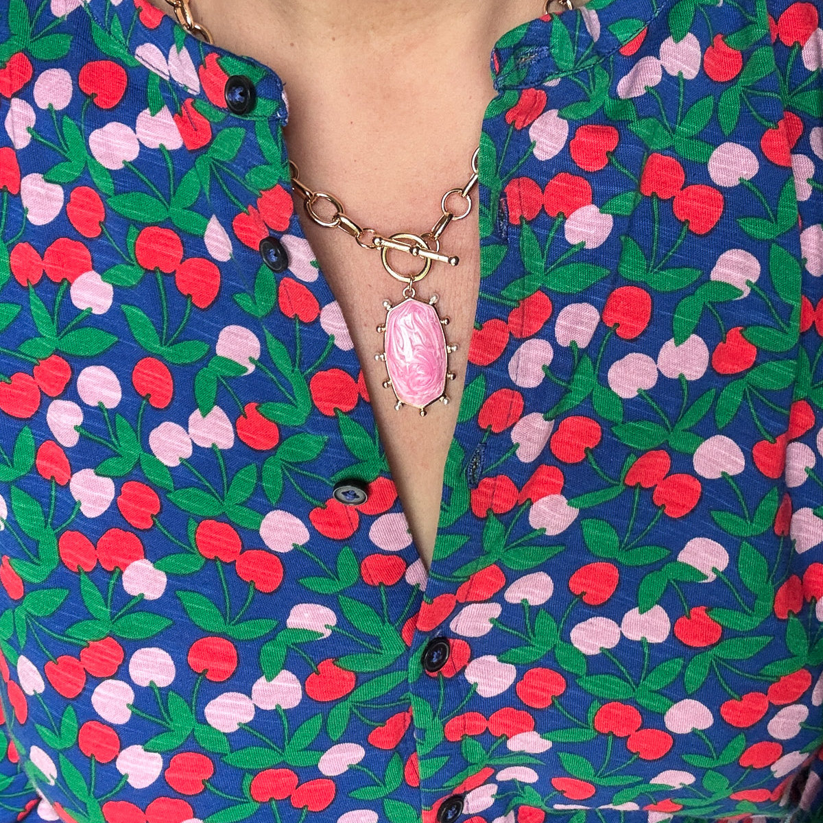 Close up of a pink marbled oval pendant on a gold chain with a toggle closure worn by a women with a colorful shirt.