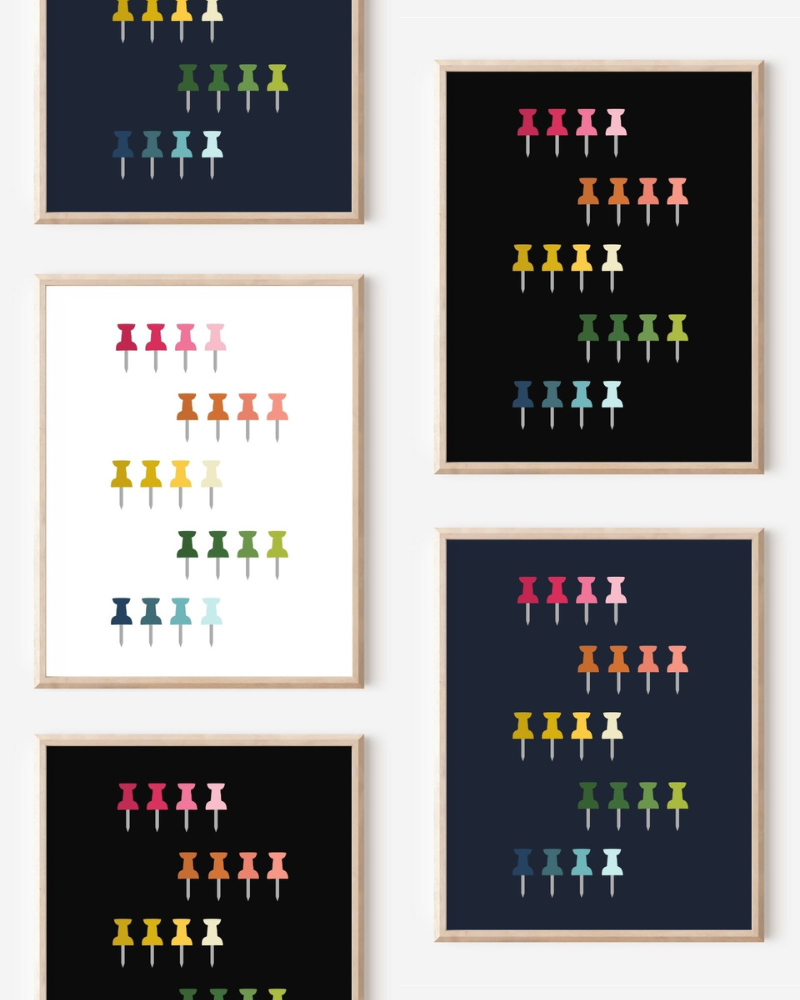 Framed art prints featuring minimalist illustrations of Push Pins in rainbow hues on black, navy blue and white backgrounds.