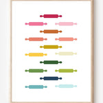 Kitchen wall art featuring rolling pins in ombre rainbow hues arranged in a grid pattern on a white background.