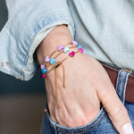 Close up of three gold adjustable bracelets with colorful enamel hearts. 