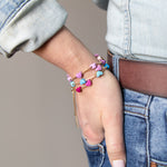 Women wearing a stack of three gold chain adjustable bracelets with colored enamel hearts in Pink, Blue and Purple.