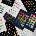 stack of rainbow graphic art prints featuring everyday objects like laundry baskets, toilet plungers, toothbrushes and scissors laid on a light gray surface