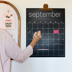 Woman writing on erasable black wall calendar with white chalk marker