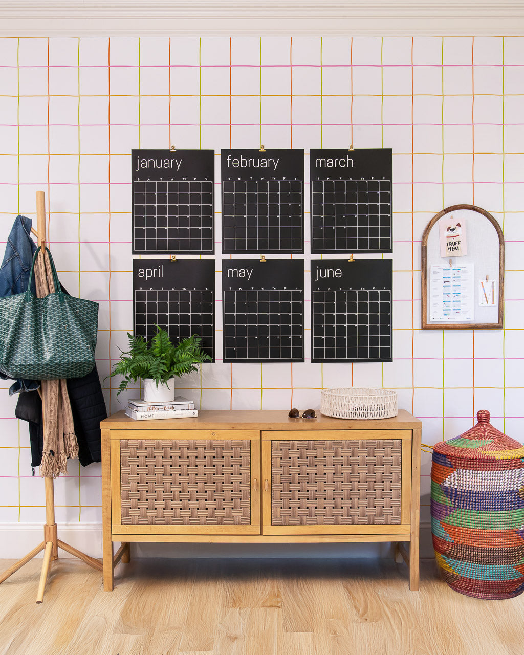 Room interior with a wooden sideboard, large black calendar on the wall, colorful basket and coat rack