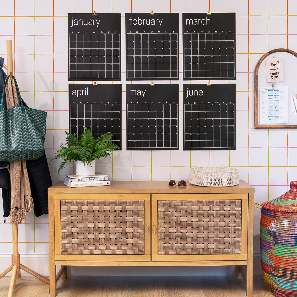 Large reusable black calendar on a wall with a wooden cabinet below and colorful decor items around.