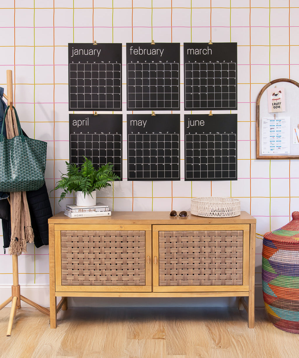 Large reusable black calendar on a wall with a wooden cabinet below and colorful decor items around.
