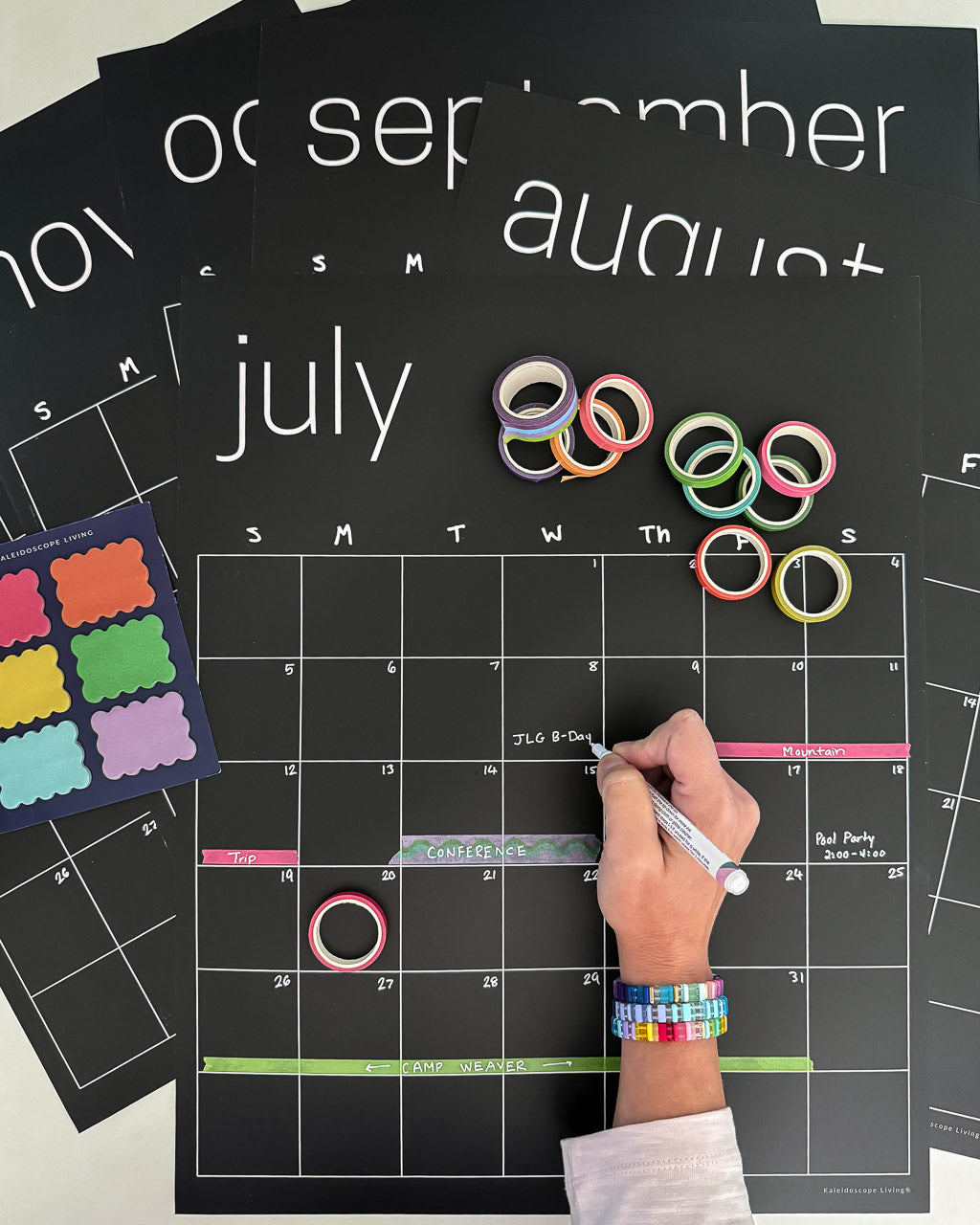Erasable black calendar with colorful washi tape and sticky notes with woman's hand writing on it in white chalk marker
