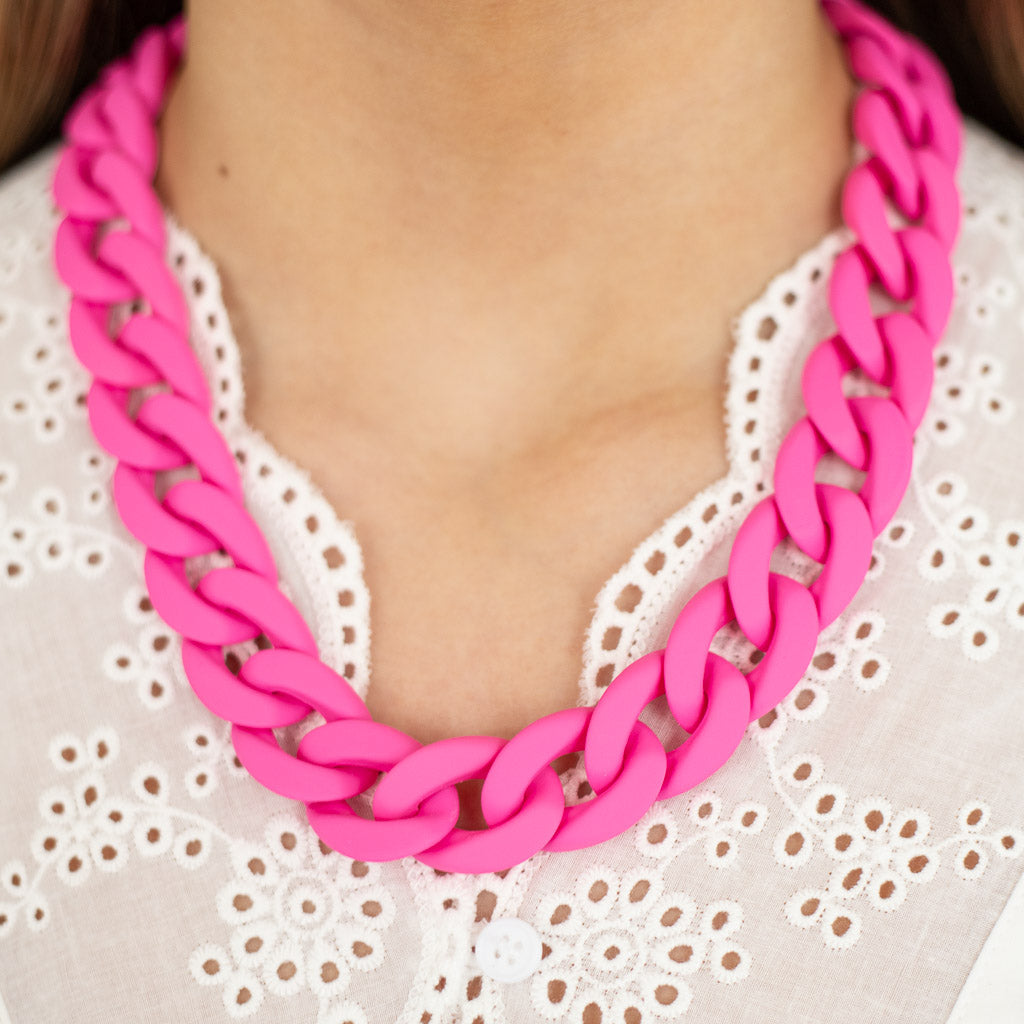 Pink acrylic link necklace worn by a women wearing a white lace top.