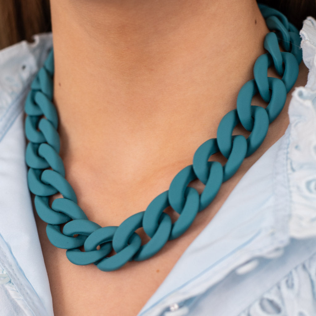Teal blue acrylic link necklace worn by a women wearing a light blue top.