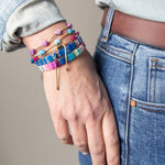 Hand wearing a stack of colorful bracelets including ones with enamel hearts and other with resin tiles.