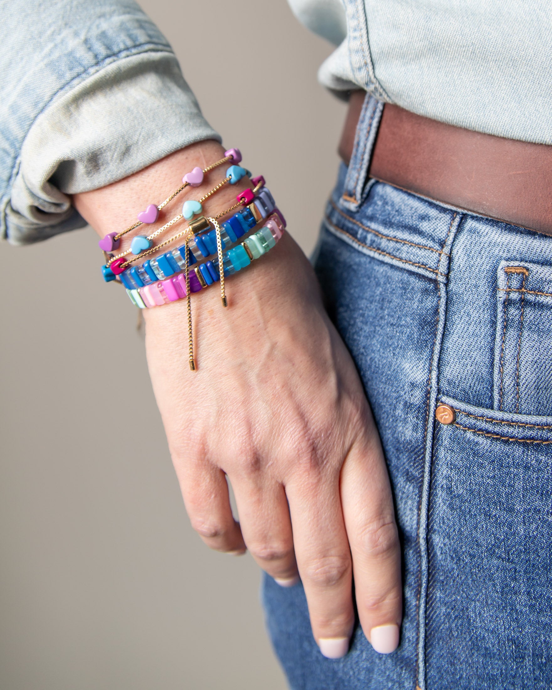 Hand wearing a stack of colorful bracelets including ones with enamel hearts and other with resin tiles.