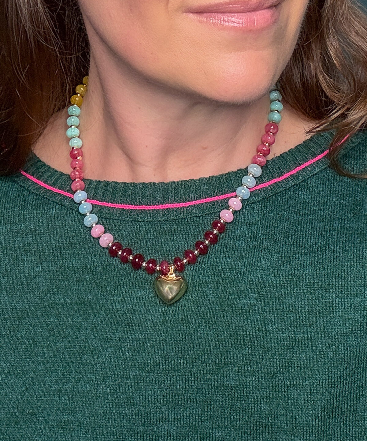 Women wearing a necklace in a blend of pink, blue, and yellow natural stone beads accented with a gold heart pendant in a green sweater.