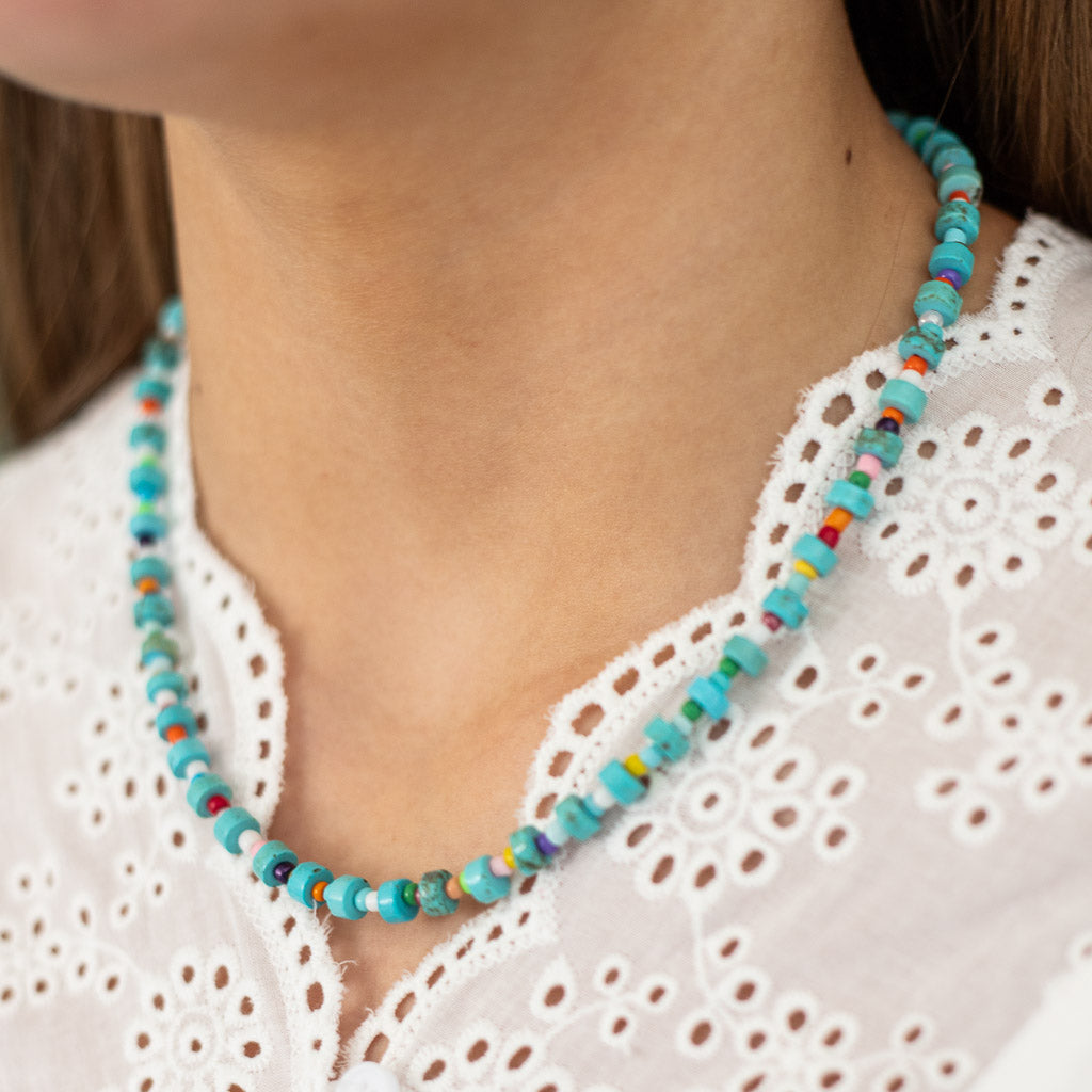 A close-up image of a person wearing a white lace top, showcasing a turquoise stone beaded necklace with colorful spacer beads.