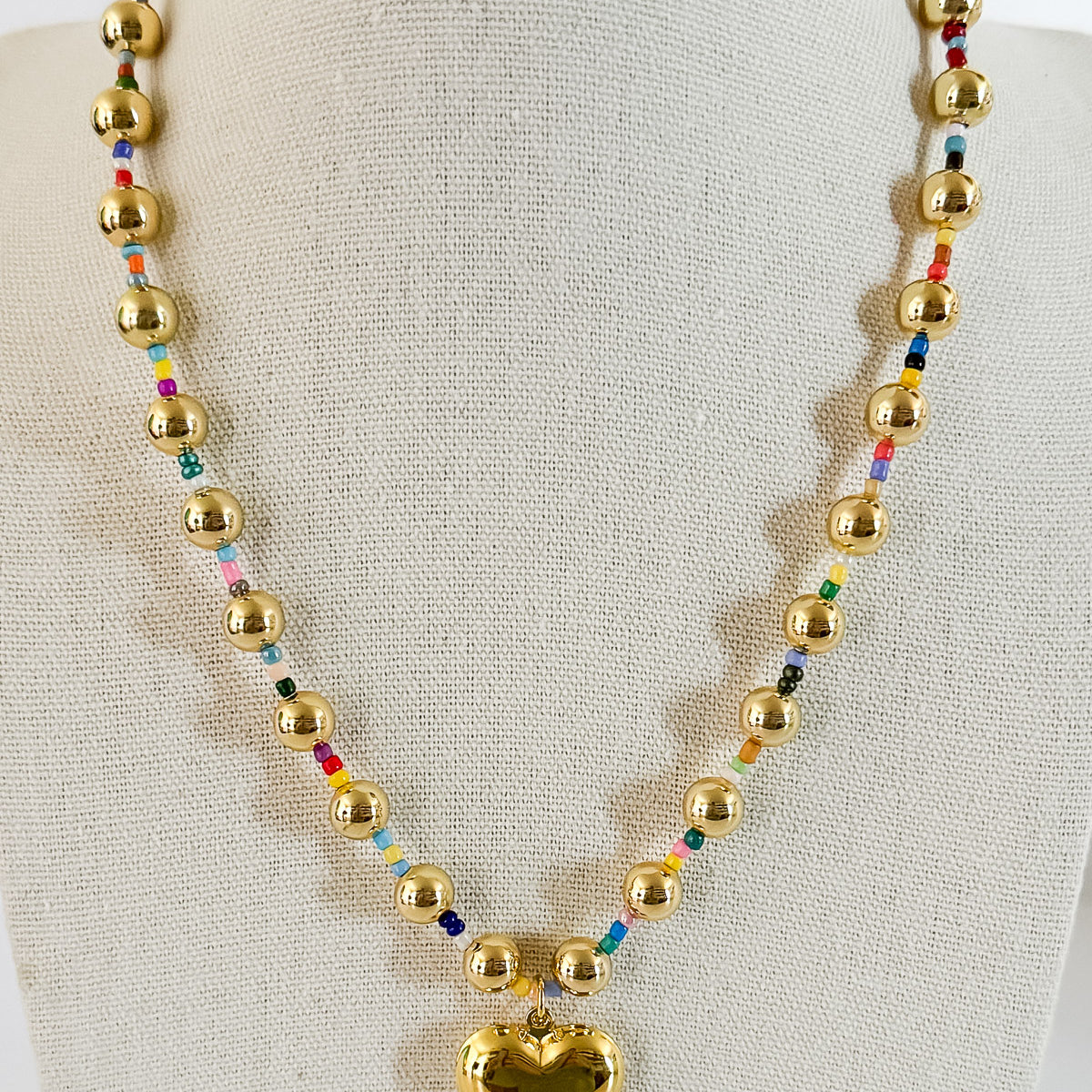 A gold-plated alloy necklace with hollow gold beads and a heart-shaped pendant, spaced with colorful beads.