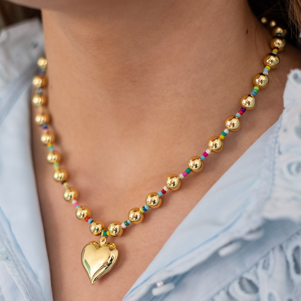 Close up of girl wearing gold beaded heart pendant necklace spaced with colorful beads.