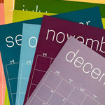 Stack of the reusable rainbow wall calendars from Kaleidoscope Living.