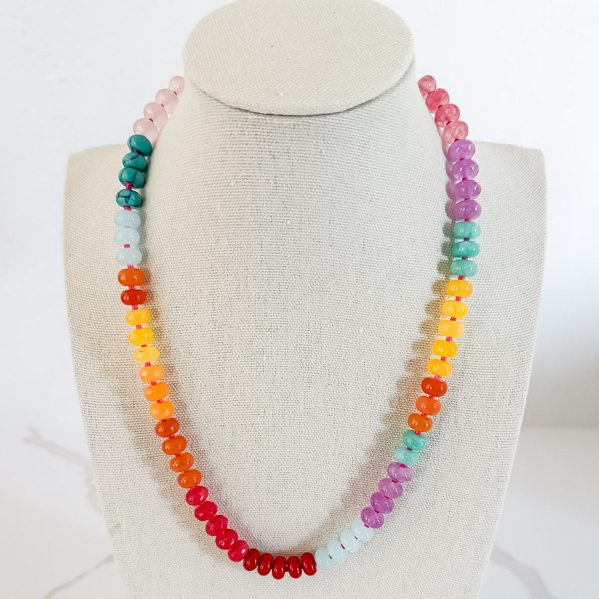 A beaded necklace with a variety of natural stone in hues of pink, yellow, orange, blue, and red, displayed on a mannequin.