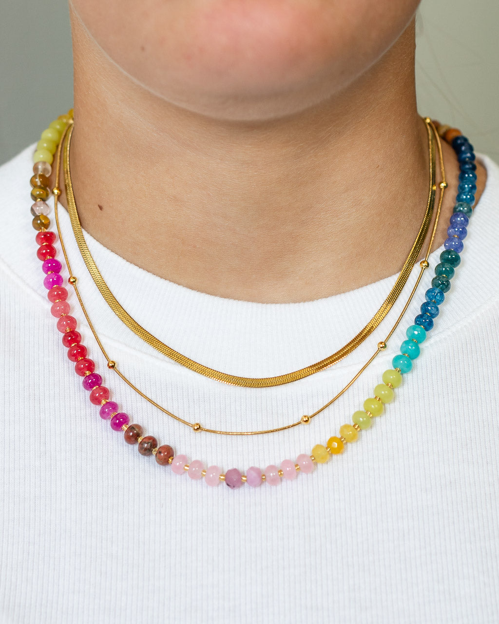 Multicolored beaded necklace in a rainbow palette layered with a gold snake chain by Kaleidoscope Living.