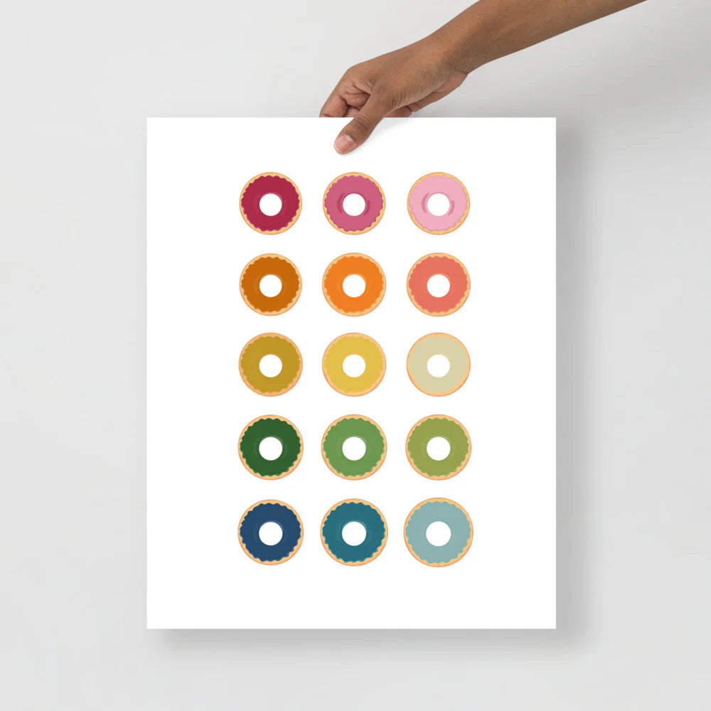 kitchen art print with a white background and grid of colorful clip art of donuts in ombre rainbow colors ranging from pinks to blues