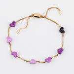 Gold adjustable bracelet with purple enamel hearts on a white background