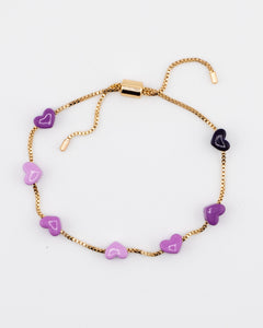 Gold adjustable bracelet with purple enamel hearts on a white background