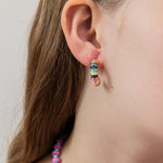 Close-up of a colorful hoop earring displaying blues, greens, orange, and yellow with gold accents.