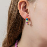 Close-up of a colorful hoop earring displaying blues, greens, orange, and yellow with gold accents.