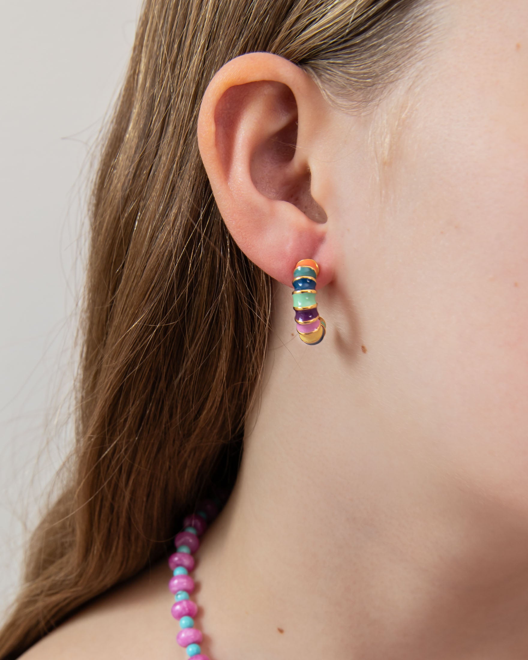Close-up of a colorful hoop earring displaying blues, greens, orange, and yellow with gold accents.