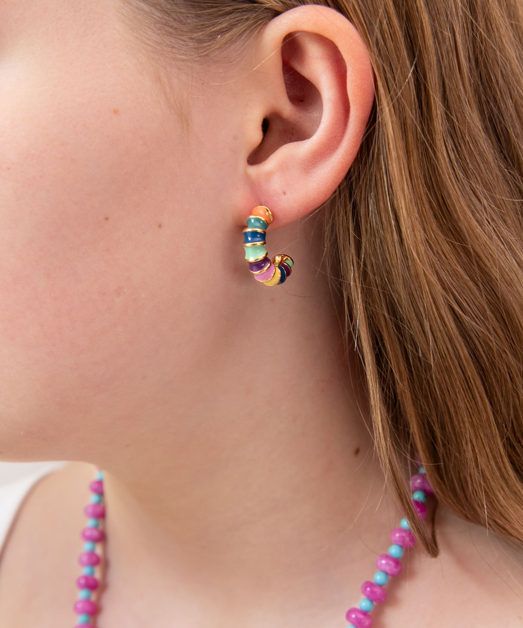Close-up of a person wearing colorful hoop earring with green, blue, yellow and gold accents.  