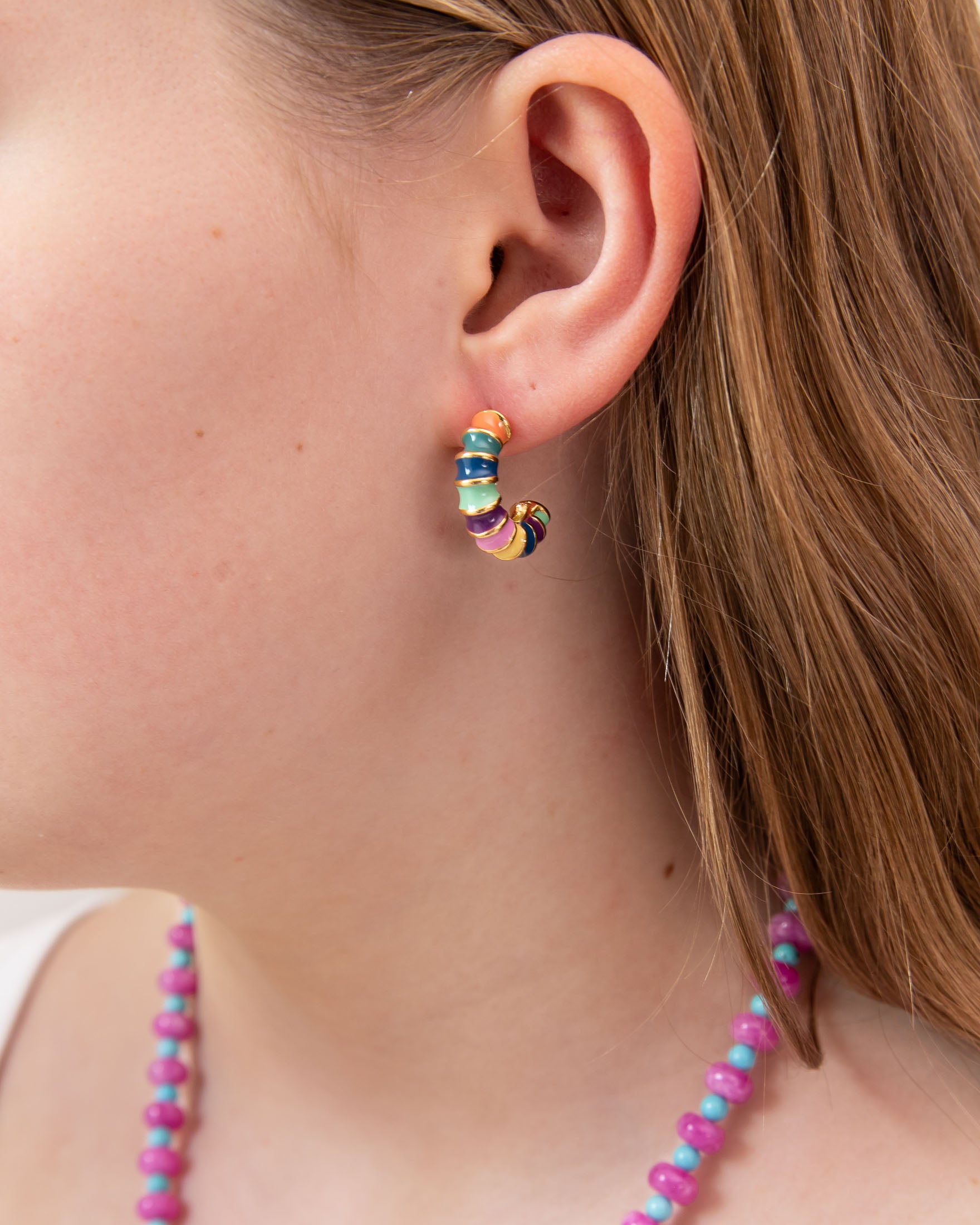 Close-up of a person wearing colorful hoop earring with green, blue, yellow and gold accents.  