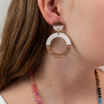 Close-up of a person wearing a white acrylic and wood hoop earring with a colorful necklace 