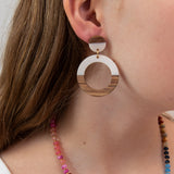 Close-up of a person wearing a white acrylic and wood hoop earring with a colorful necklace 