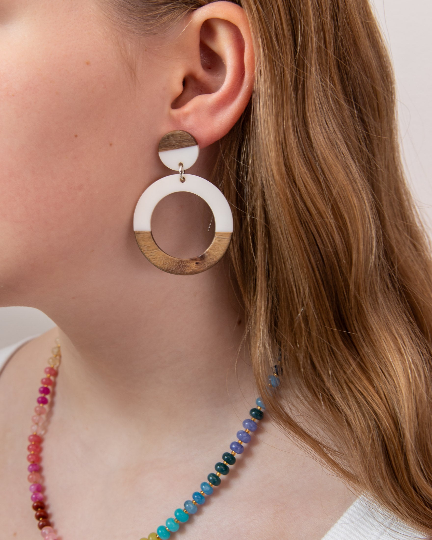 Close-up of a girl wearing wood and white resin hoop earring with a colorful beaded necklace by Kaleidoscope Living