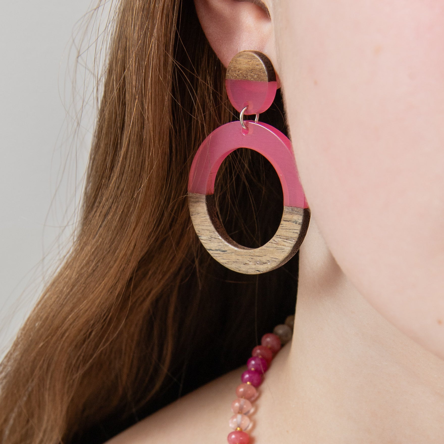 Close-up of a person wearing pink resin  and wood hoop earring by Kaleidoscope Living