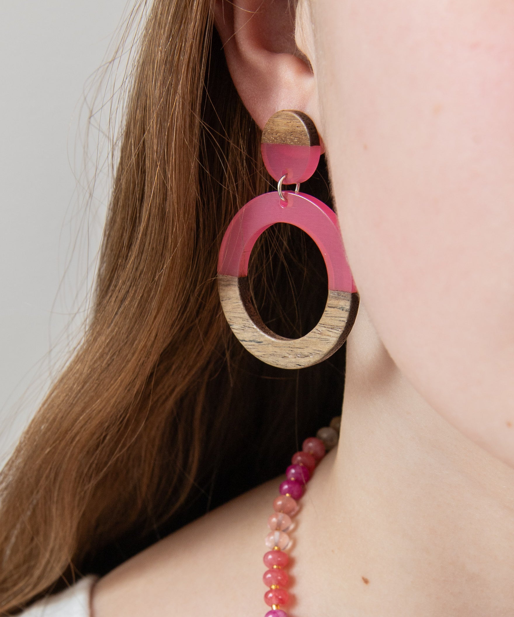 Close-up of a person wearing pink resin  and wood hoop earring by Kaleidoscope Living