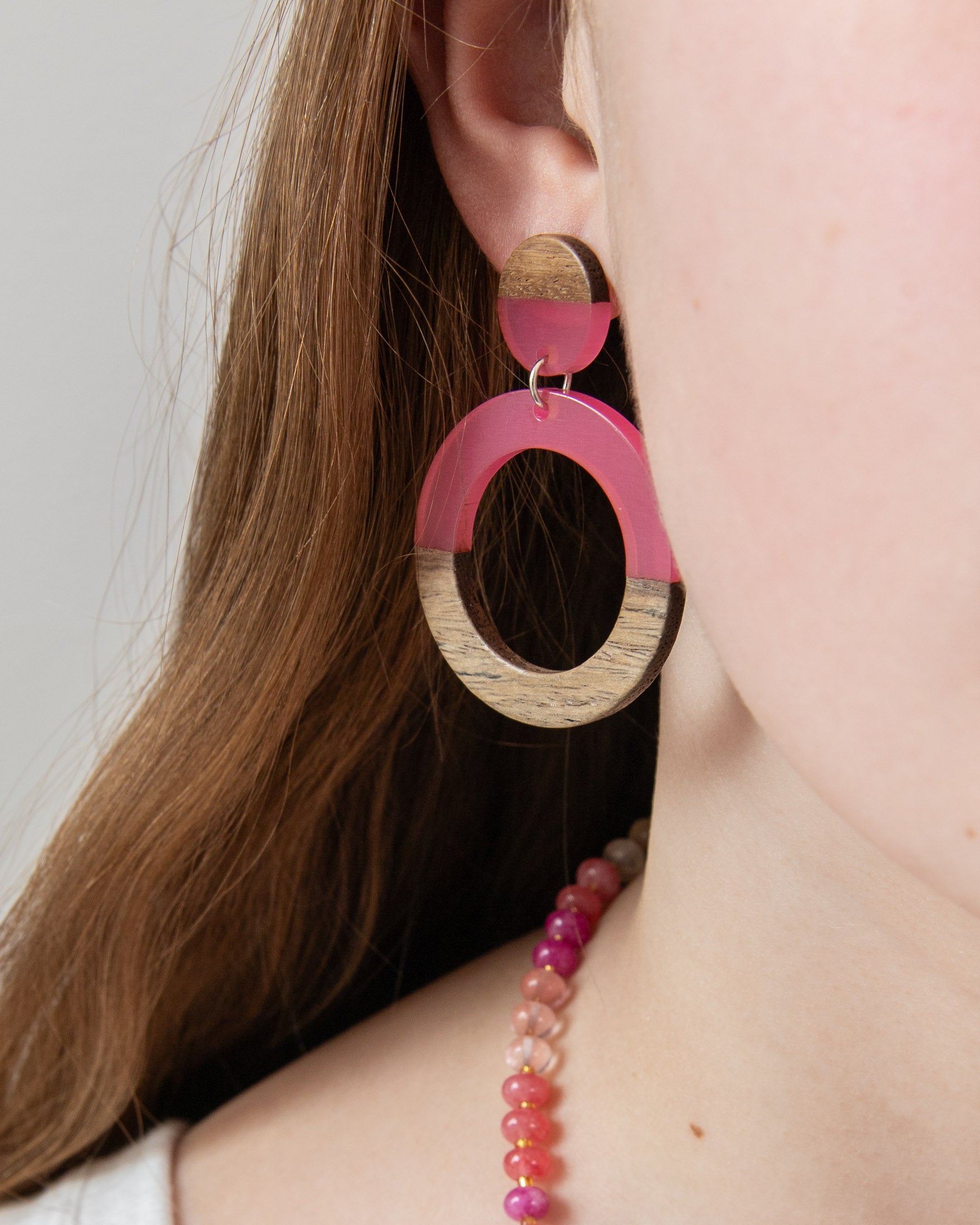 Close-up of a person wearing pink resin  and wood hoop earring by Kaleidoscope Living