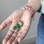 Set of green hoop earrings held in a hand with colorful bracelets by Kaleidoscope Living.