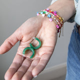 Set of green hoop earrings held in a hand with colorful bracelets by Kaleidoscope Living.