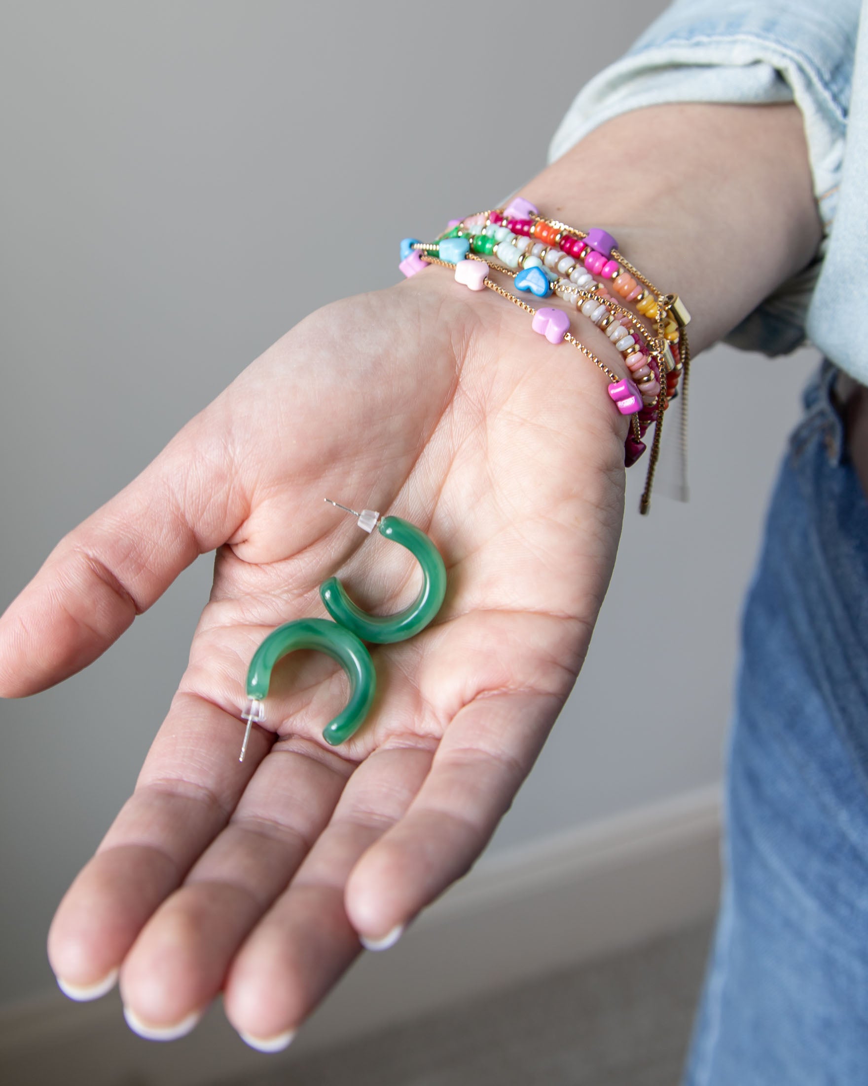 Set of green hoop earrings held in a hand with colorful bracelets by Kaleidoscope Living.