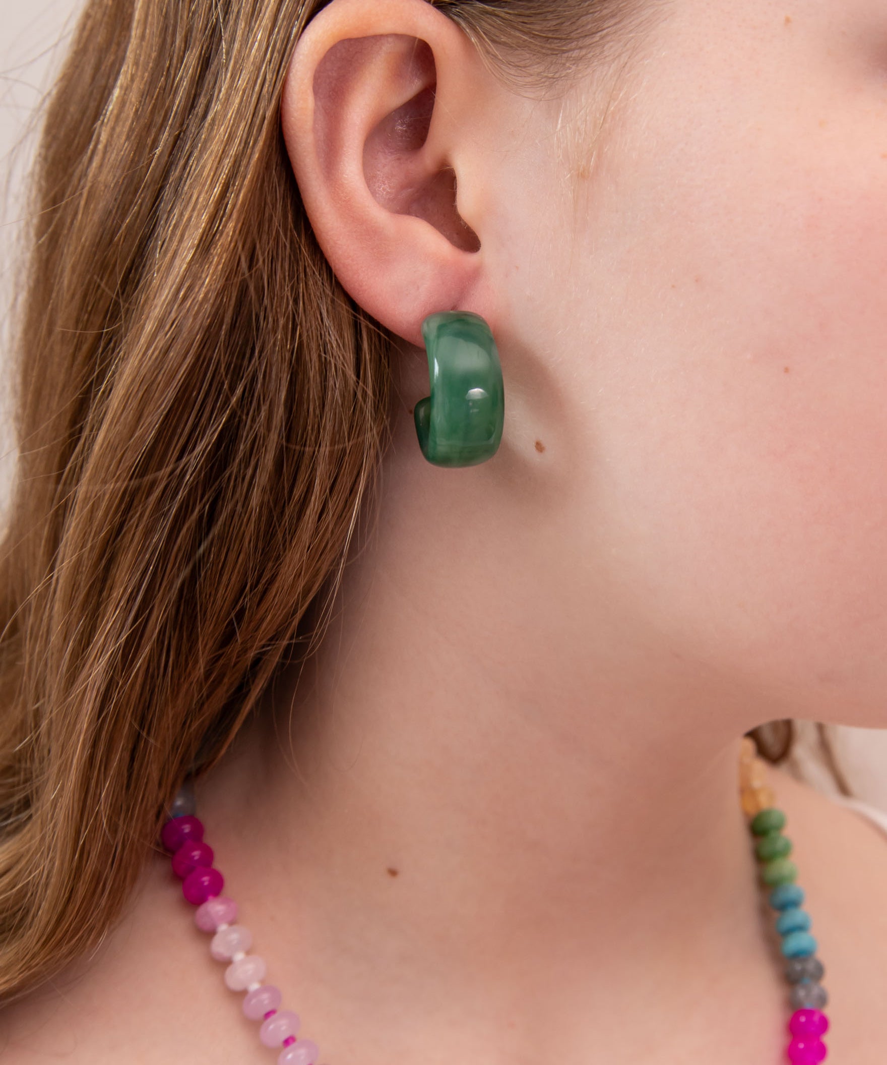Close-up of a girl wearing a green acrylic hoop earring with colorful beads around her neck.