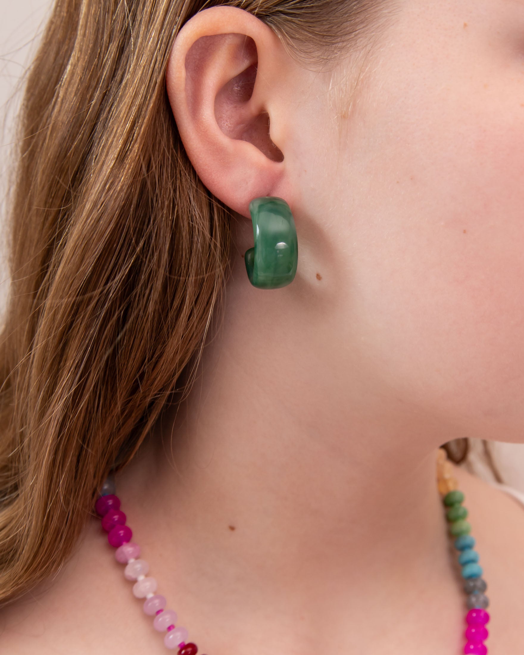 Close-up of a girl wearing a green acrylic hoop earring with colorful beads around her neck.