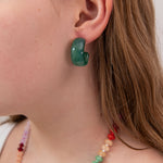 Close-up of a girl wearing a green acrylic hoop earring with a plain background