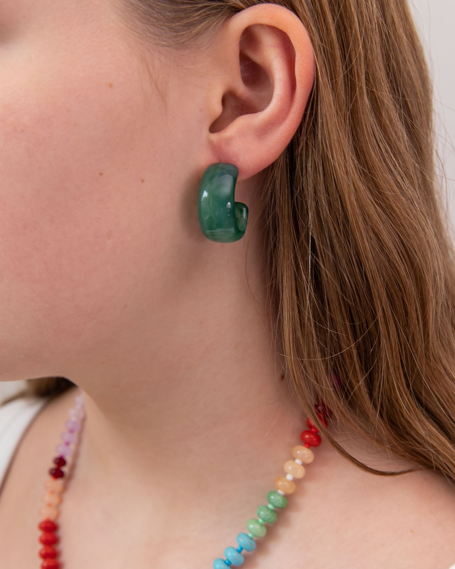 Close-up of a girl wearing a green acrylic hoop earring with a plain background