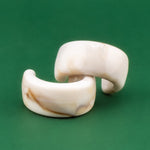 Pair of acrylic cream tortoiseshell earrings on a green background