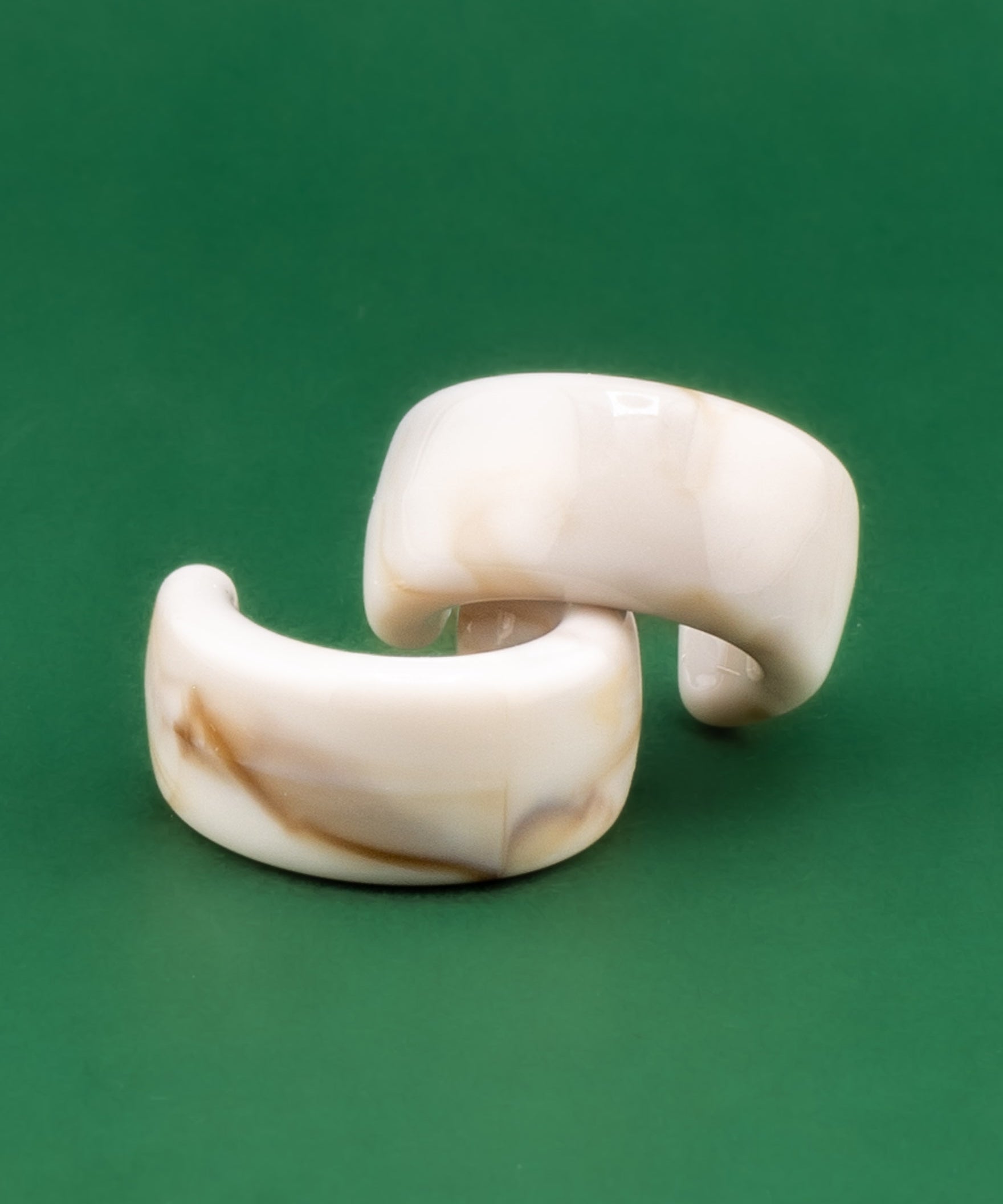 Pair of acrylic cream tortoiseshell earrings on a green background